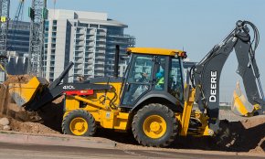 A 410L Backhoe Loader works with an apartment complex in the background