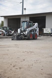 Bobcat planer attachment mounted to a skid-steer loader cuts an asphalt parking lot.