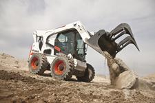 Bobcat S850 M2-Series skid-steer loader empties concrete material on a construction jobsite with a grapple attachment.