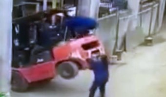 The woman jumps on the back of the forklift to pull it back down as it starts to tip