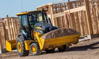 Tractor Loader hauling a bucket full of dirt through a residential job site